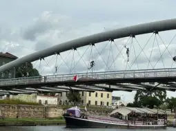 Most z łodzią na rzece, w tle budynki i chmury.