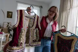 Kobieta trzyma dwie haftowane kamizelki w kolorze czerwonym i granatowym.