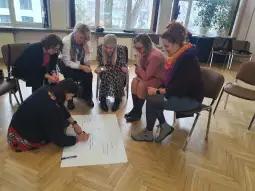 Grupa osób pracujących wspólnie nad dużym arkuszem papieru w sali konferencyjnej.