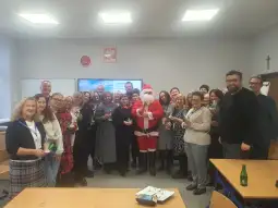 Grupa ludzi w strojach świątecznych, w tym Mikołaj, trzymających prezenty.