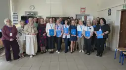 Grupa osób z dyplomami w sali, uśmiechnięte twarze, różnorodne stroje.