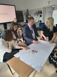 Grupa osób pracuje nad projektem, używając markerów i dużego arkusza papieru.