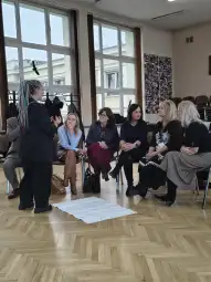 Grupa kobiet w trakcie dyskusji w sali, jedna z nich prowadzi rozmowę.