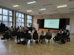 Spotkanie grupy ludzi w sali, z prezentacją na ekranie.