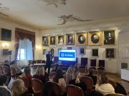 Prezentacja w sali z portretami historycznymi, uczestnicy siedzą na krzesłach.