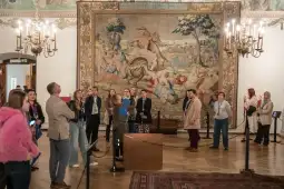 Grupa ludzi ogląda gobelin w muzeum.