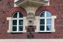 Detale architektoniczne budynku z rzeźbą lwa i oknami w stylu neorenesansowym.