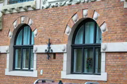 Ceglana elewacja budynku z dużymi oknami i dekoracyjnymi detalami architektonicznymi.
