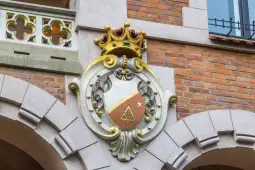 Herb z koroną i symbolami na tle ceglanej ściany.