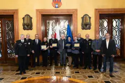 Grupa ludzi w mundurach i garniturach z dyplomami w eleganckim wnętrzu.