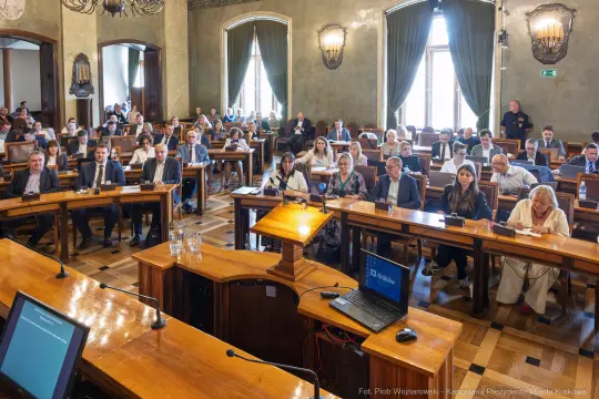 Sala obrad z uczestnikami na spotkaniu, stoły i ekrany prezentacyjne.