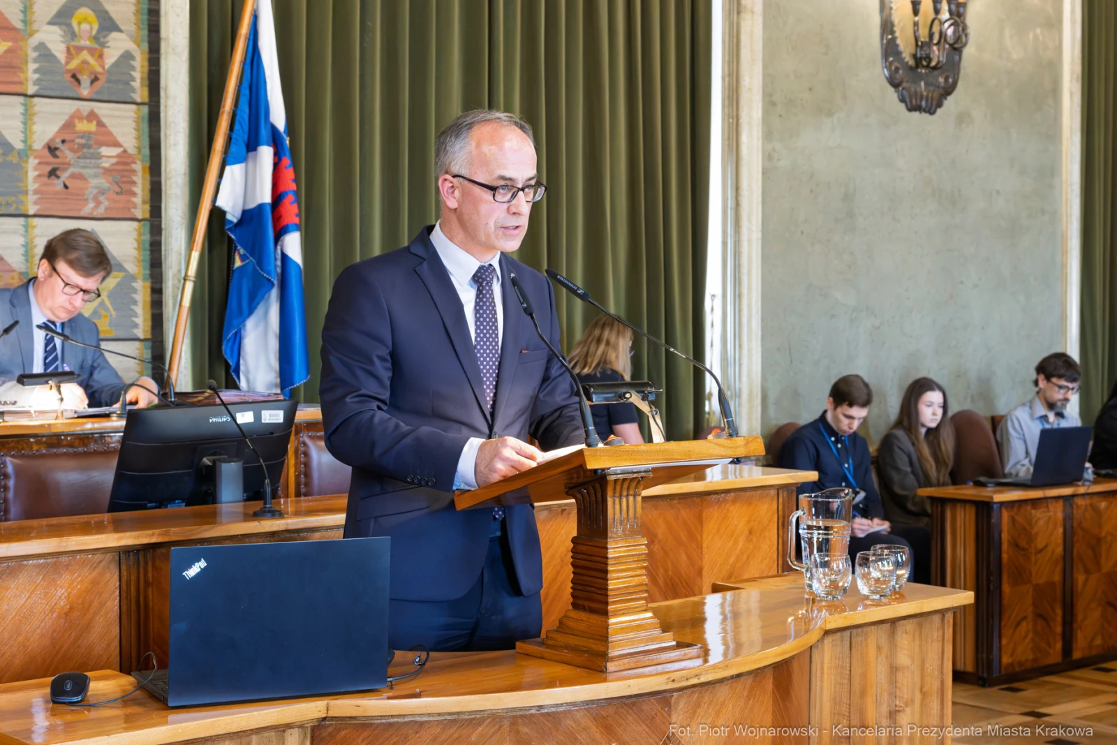 Mężczyzna w garniturze przemawia w sali obrad, w tle siedzą inni uczestnicy spotkania.  Autor: Piotr Wojnarowski