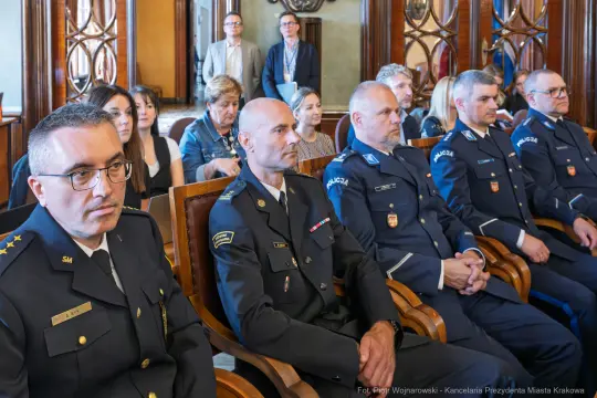 Uczestnicy ceremonii w sali, w tym przedstawiciele służb mundurowych.