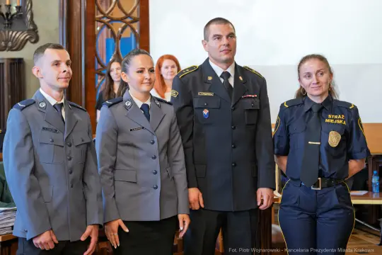 Cztery osoby w mundurach, w tym policjant i strażnik miejski, podczas uroczystości.