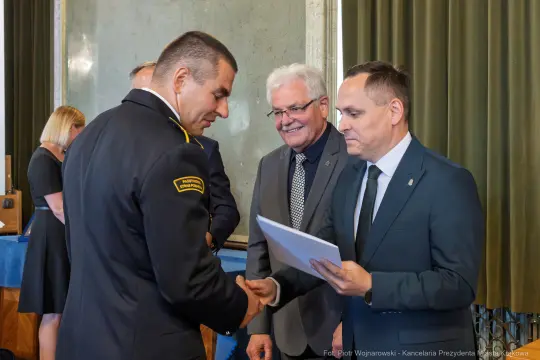 Uroczystość wręczenia nagrody z udziałem mężczyzn w mundurach i garniturach.