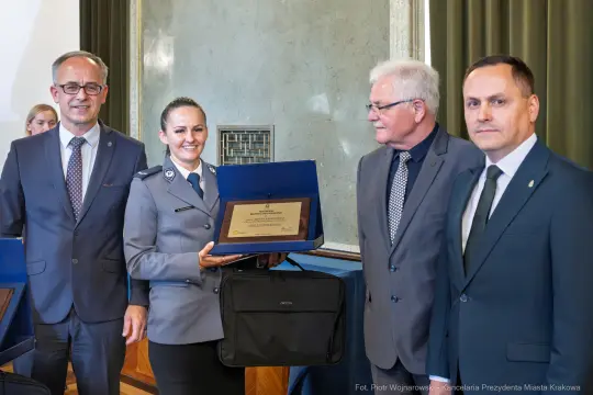 Wręczenie nagrody przez urzędników, uśmiechnięta policjantka z dyplomem.