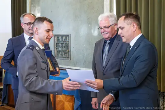 Wręczenie dyplomu przez urzędników, mężczyzna w mundurze odbiera dokument.