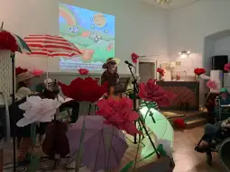 Występ artysty na scenie z kolorowymi parasolkami i dużymi kwiatami w tle.
