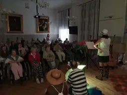 Występ artystyczny dla seniorów w sali z widownią na wózkach inwalidzkich.