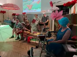 Grupa osób w strojach letnich grających na instrumentach w kolorowej scenerii.