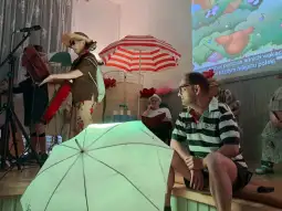 Osoby na scenie podczas występu artystycznego, z parasolami i instrumentami muzycznymi.