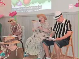 Starsze osoby w kapeluszach recytują teksty podczas letniego wydarzenia.