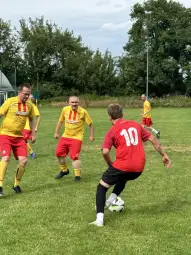 Mężczyźni grają w piłkę nożną na trawie, w różnych kolorach strojów sportowych.