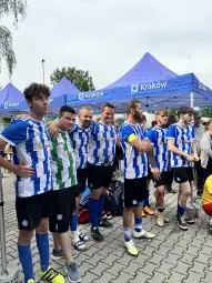 Grupa zawodników w niebiesko-białych strojach piłkarskich, stojących pod namiotami.