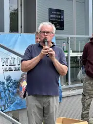 Mężczyzna z mikrofonem przemawia podczas wydarzenia na świeżym powietrzu.
