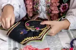 Ręczne haftowanie na czarnym materiale z kolorowymi wzorami.