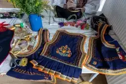 Tradycyjne haftowane kamizelki na stole, obok akcesoria do szycia i kwiaty.