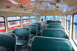 Wnętrze autobusu z zielonymi siedzeniami i metalowymi ramami.