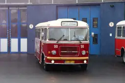 Czerwony autobus MPK z Krakowa, stojący przed budynkiem w deszczowej aurze.