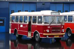 Czerwony autobus z numerem 90, stojący przed niebieską halą.