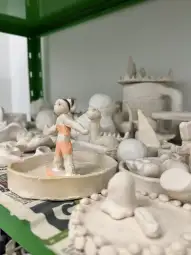 Figurka z gliny w stroju kąpielowym na tle innych rzeźb.
