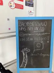 Tablica informacyjna z napisem o obserwowaniu na Instagramie oraz rysunkiem żyrafy.