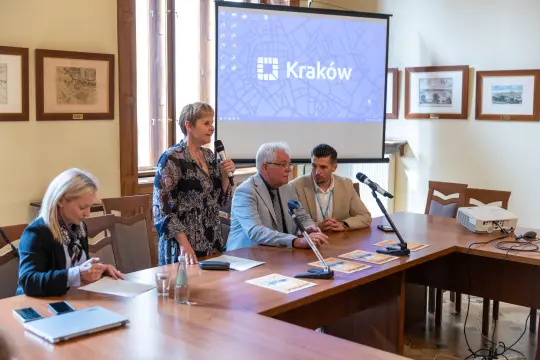 Konferencja w Krakowie, prelegenci przy stole, prezentacja na ekranie.