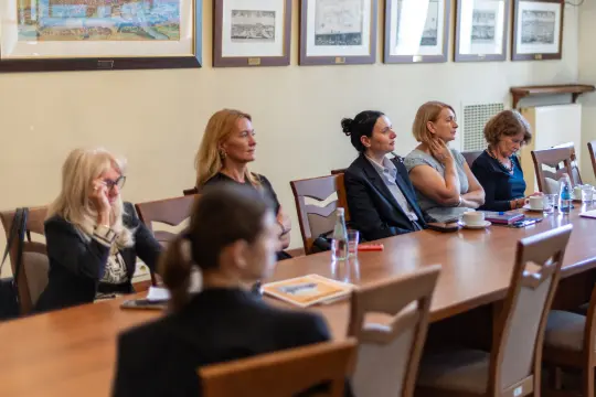 Grupa kobiet w formalnych strojach siedzi przy stole w sali konferencyjnej.