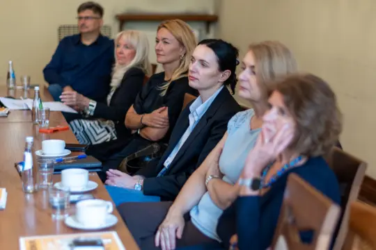 Grupa osób siedzących przy stole, skupionych na prezentacji lub dyskusji.