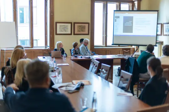 Spotkanie w sali konferencyjnej z prezentacją na ekranie i uczestnikami przy stole.