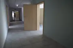 Pusty korytarz z otwartymi drzwiami i jasnym oświetleniem.