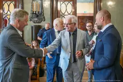 Spotkanie dwóch mężczyzn na tle eleganckiego wnętrza, wśród innych uczestników.