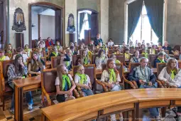 Grupa dzieci w sali obrad, siedzących w rzędach, z zielonymi chustami na szyjach.