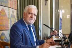 Mężczyzna w garniturze siedzący przy stole, uśmiechający się do kamery.
