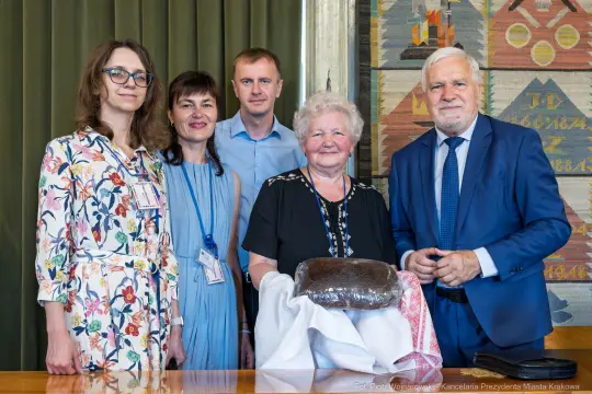 Grupa osób pozująca z tortem w ceremonialnym otoczeniu.