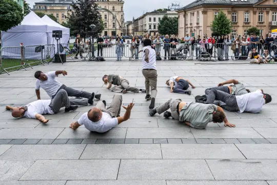 Grupa tancerzy wykonujących choreografię na placu, widownia obserwująca z boku.