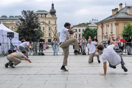 Grupa tancerzy wykonujących choreografię na placu w mieście.