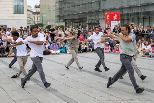 Grupa tancerzy wykonujących choreografię na placu wśród widowni.