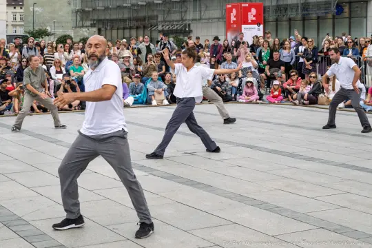 Grupa tancerzy wykonujących układ taneczny na placu, w tle widownia.