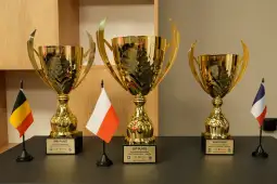 Trzy puchary z oznaczeniami 1. miejsce, 2. miejsce i 3. miejsce oraz flagi Polski, Niemiec i Francji.